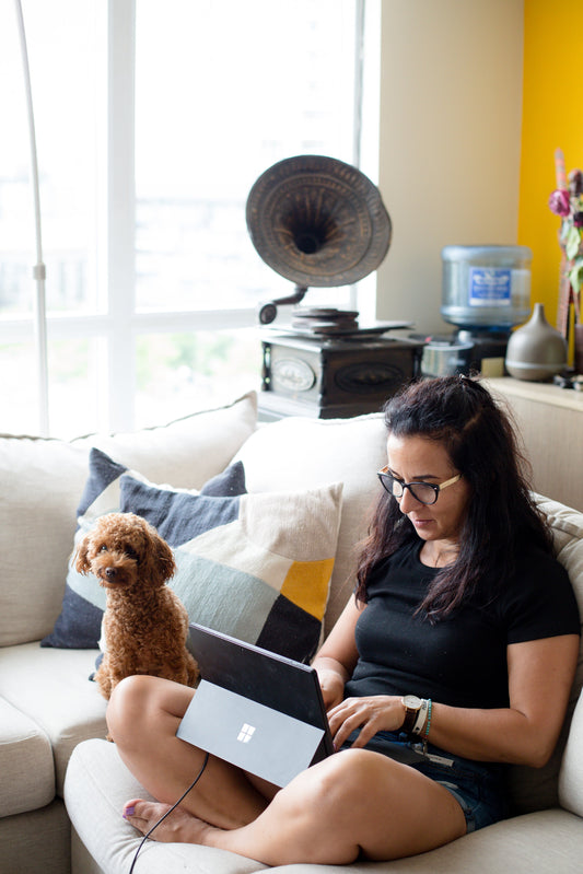 Person sitting on a sofa enjoying with her dog and using a laptop